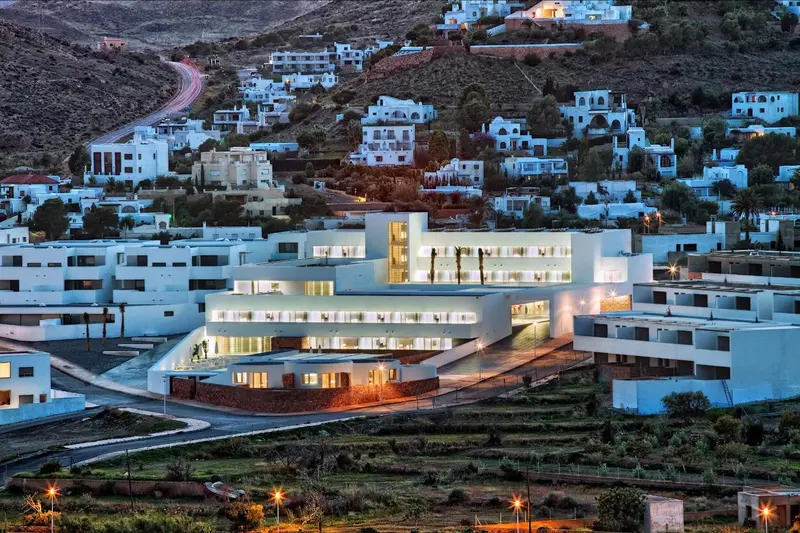 Vue d'ensemble d'un complexe hôtelier blanc illuminé au crépuscule, niché sur une colline.
