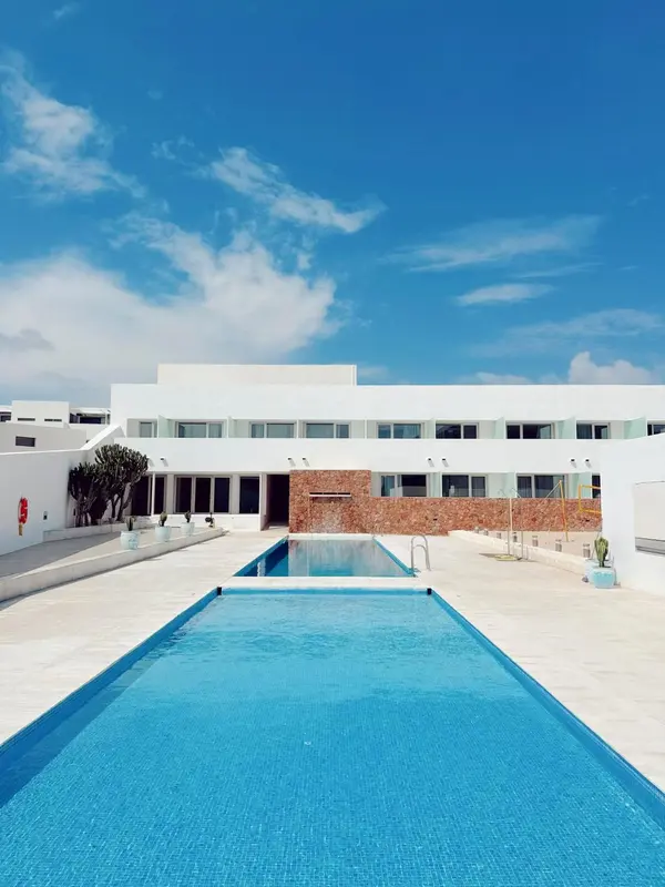 Une piscine rectangulaire turquoise est au premier plan devant un bâtiment blanc moderne.