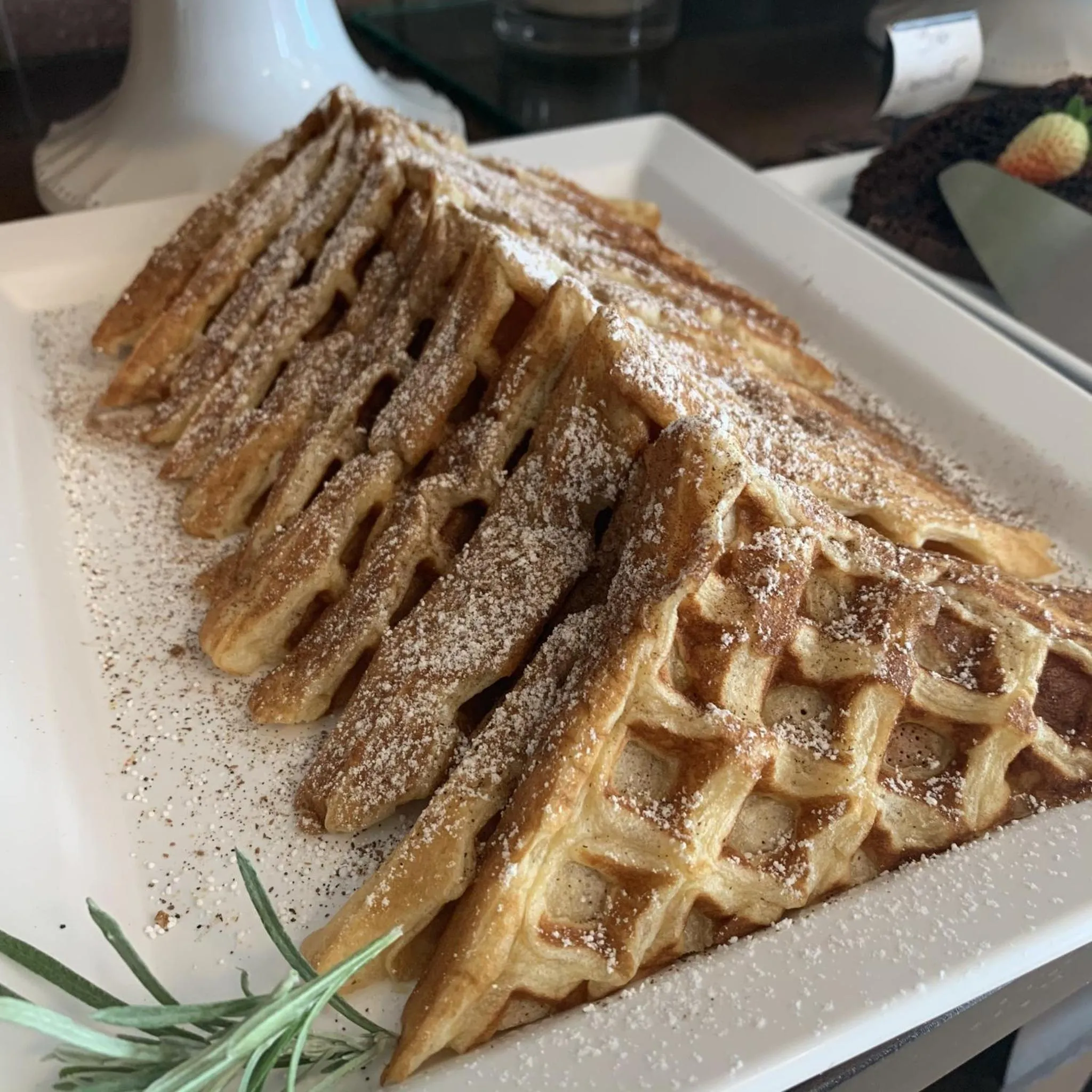 Une pile de gaufres saupoudrées de sucre glace est présentée sur une assiette blanche.