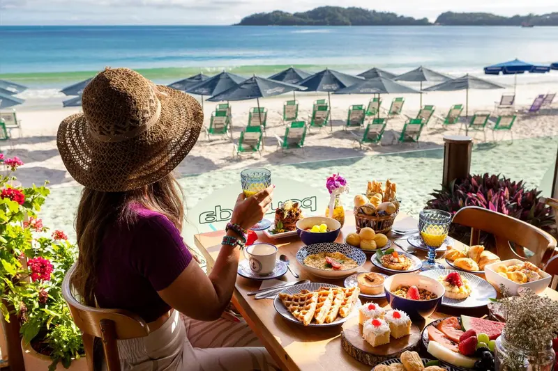 Une personne déguste un petit-déjeuner face à une plage ensoleillée.