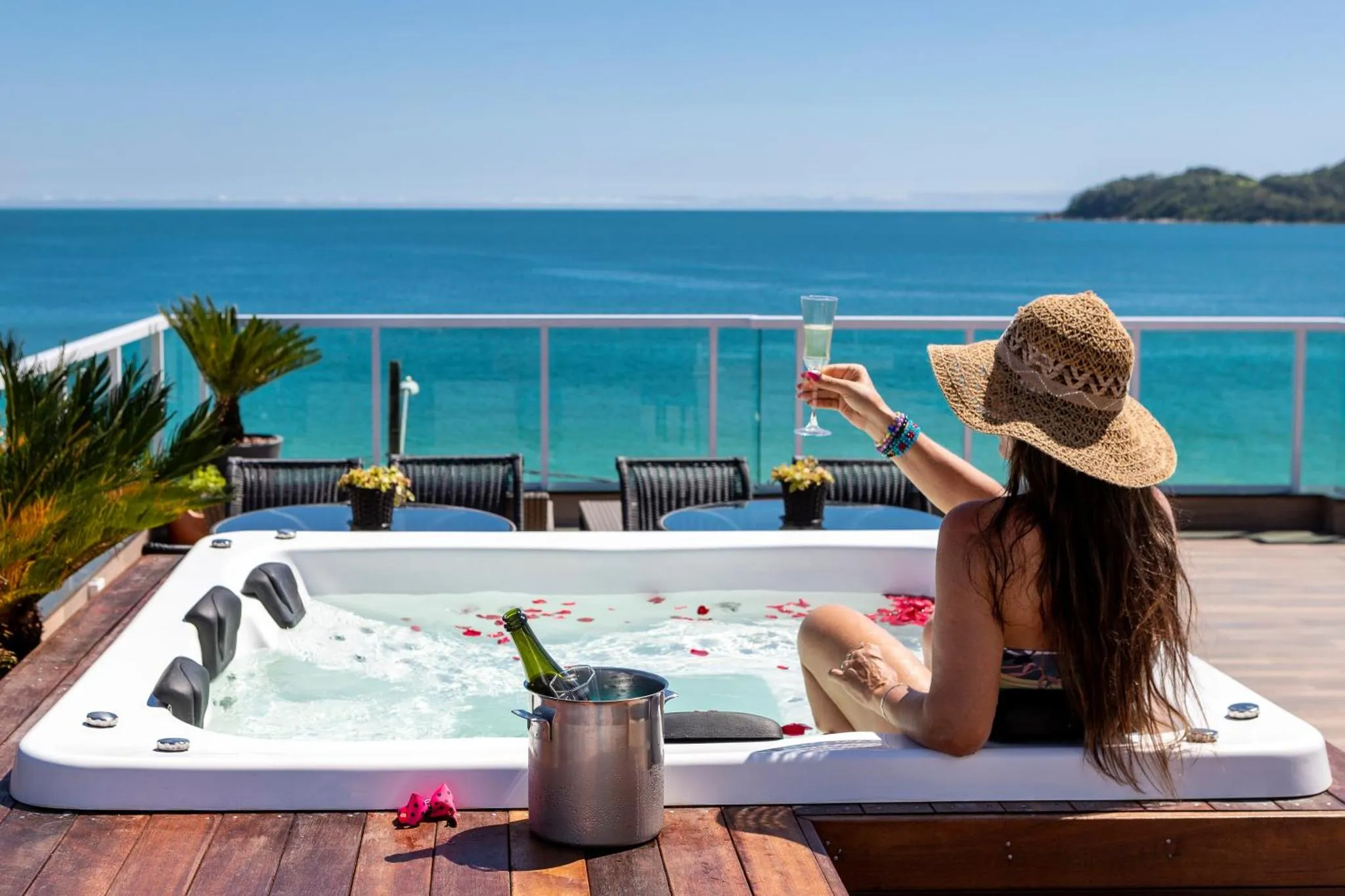 Une personne se détend dans un jacuzzi avec une boisson, face à la mer.