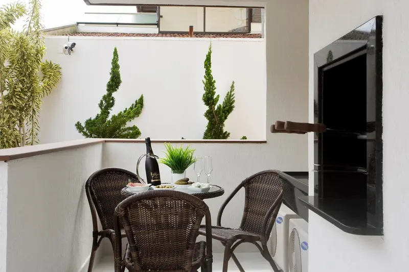 Une table et des chaises en rotin sont disposées sur un balcon avec une plante et un barbecue.