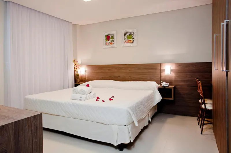 Une chambre lumineuse avec un grand lit recouvert d'une couette blanche et décoré de pétales de fleurs.