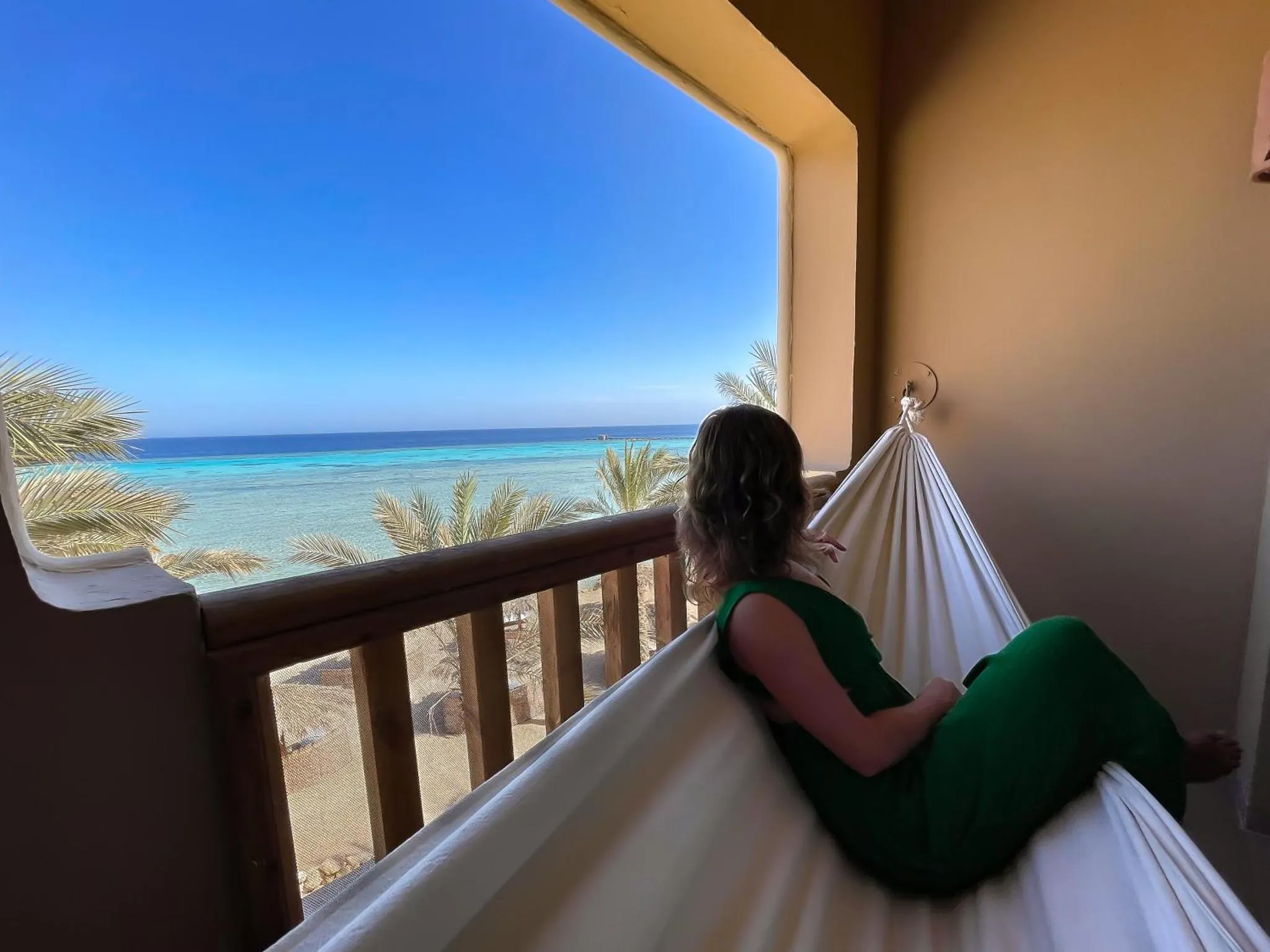 Une personne se détend dans un hamac sur une terrasse avec vue sur la mer.