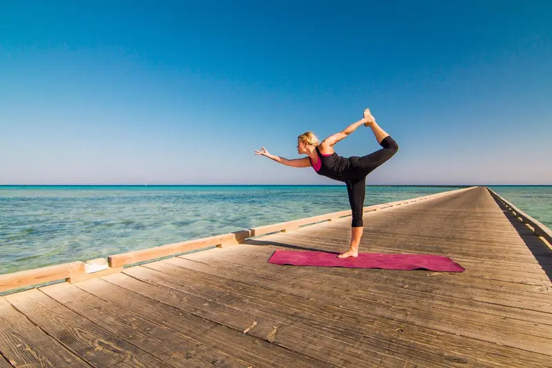 Une femme pratique le yoga sur un ponton en bois au-dessus de l'eau.