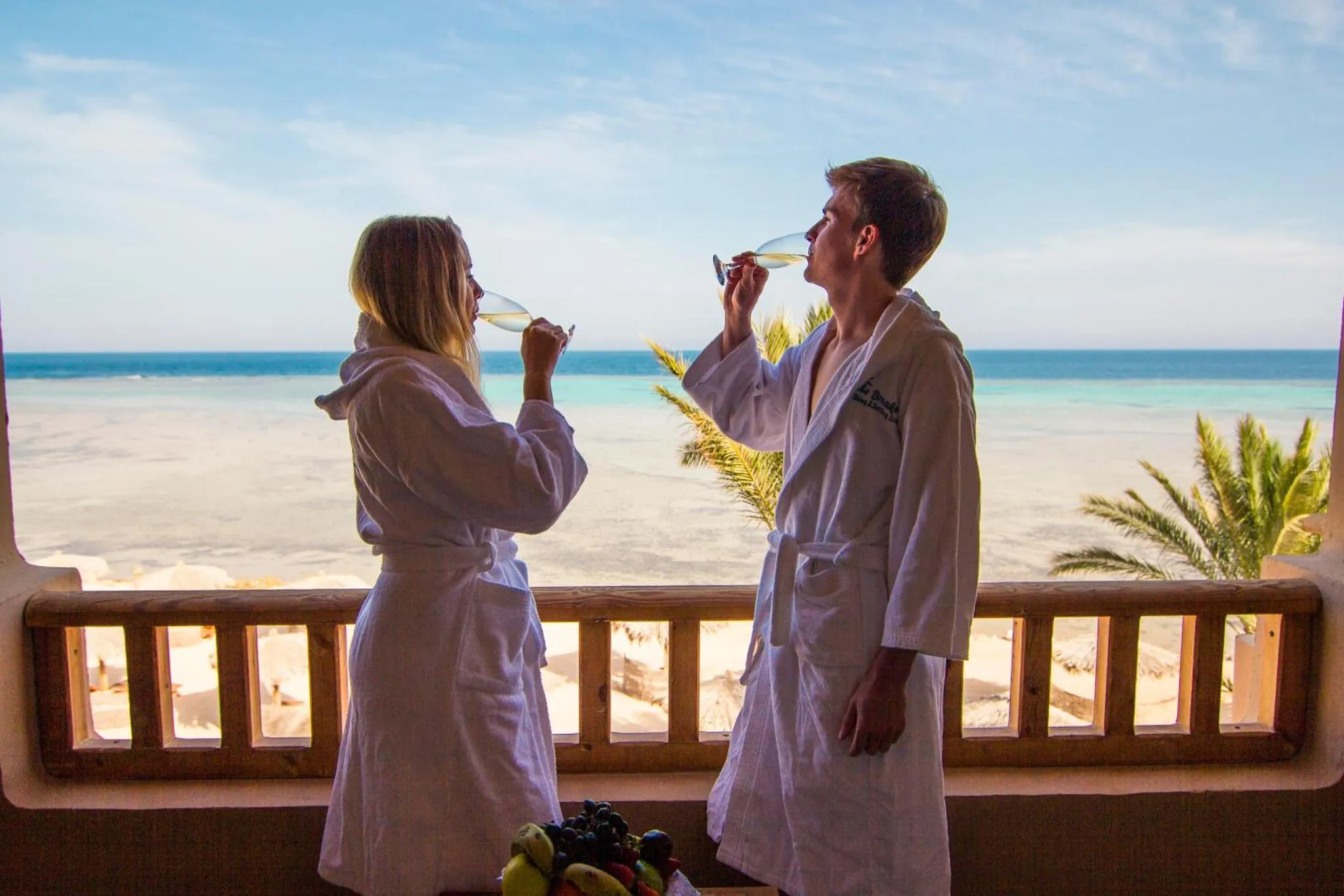Un couple porte des toasts sur une terrasse ensoleillée avec vue sur la mer.