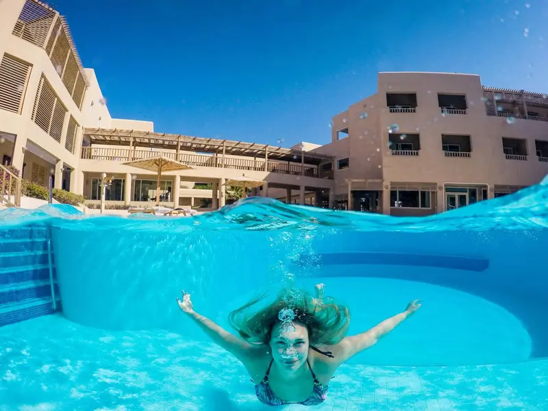 Une femme nage sous la surface de l'eau dans une piscine ensoleillée.