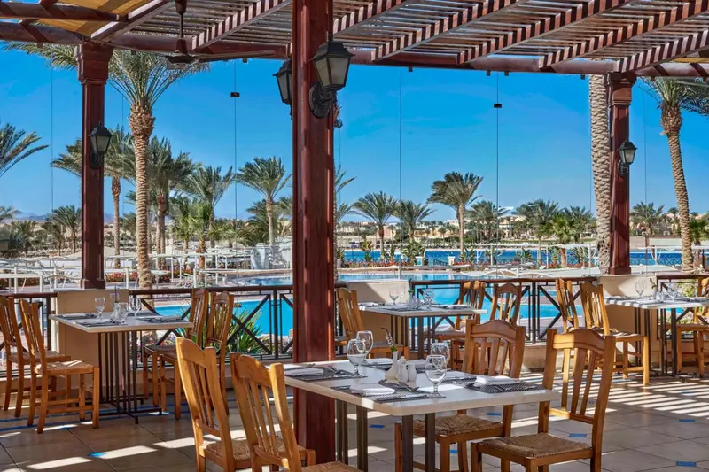 Terrasse ombragée avec tables et chaises près d'une piscine.