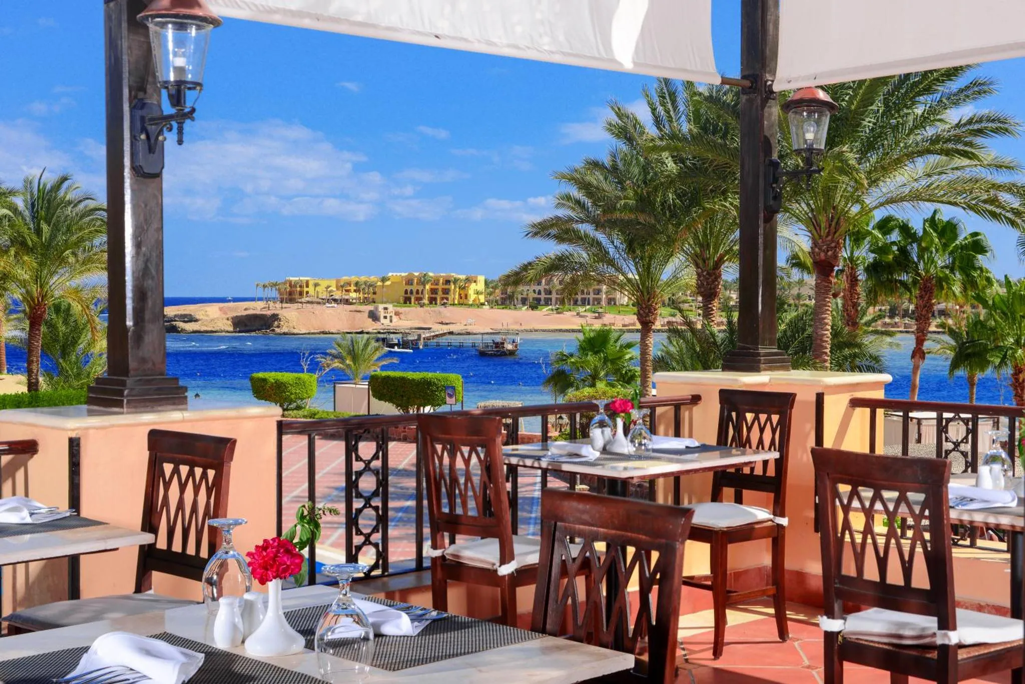 Tables dressées sur une terrasse ombragée avec vue sur la mer et la végétation.