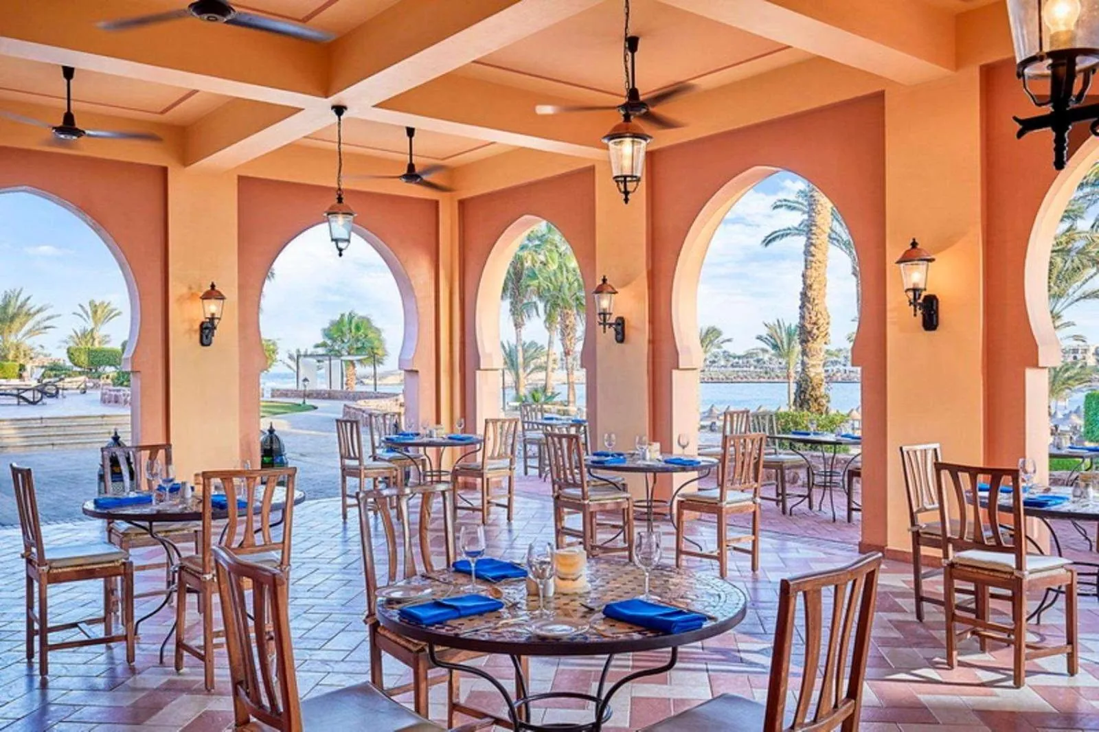 Terrasse ombragée avec tables et chaises donnant sur la mer.