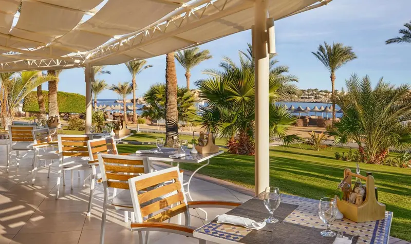 Terrasse ombragée avec tables et chaises près d'une plage de sable.