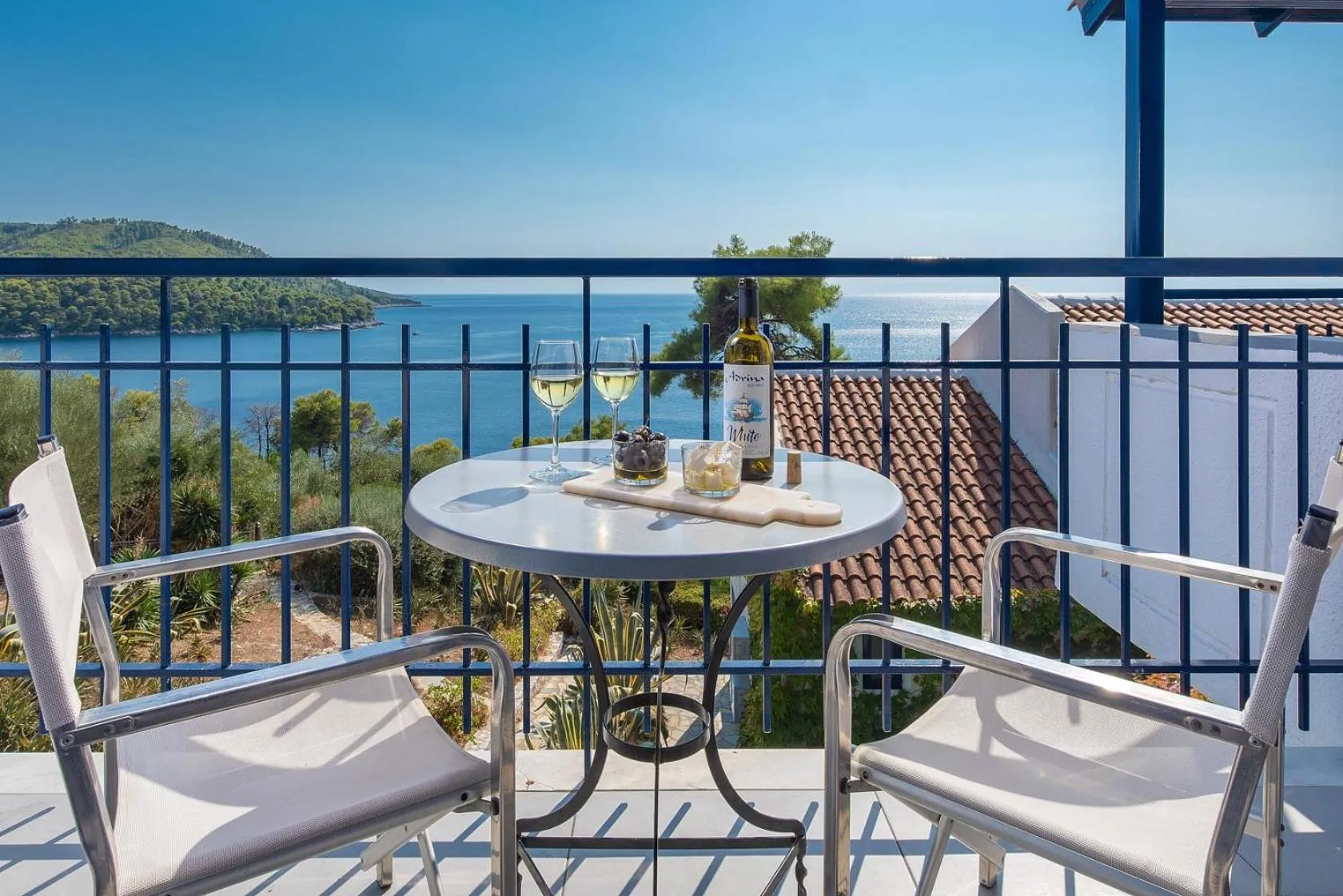 Une table ronde avec deux verres de vin et une bouteille sur une terrasse ensoleillée avec vue sur la mer.