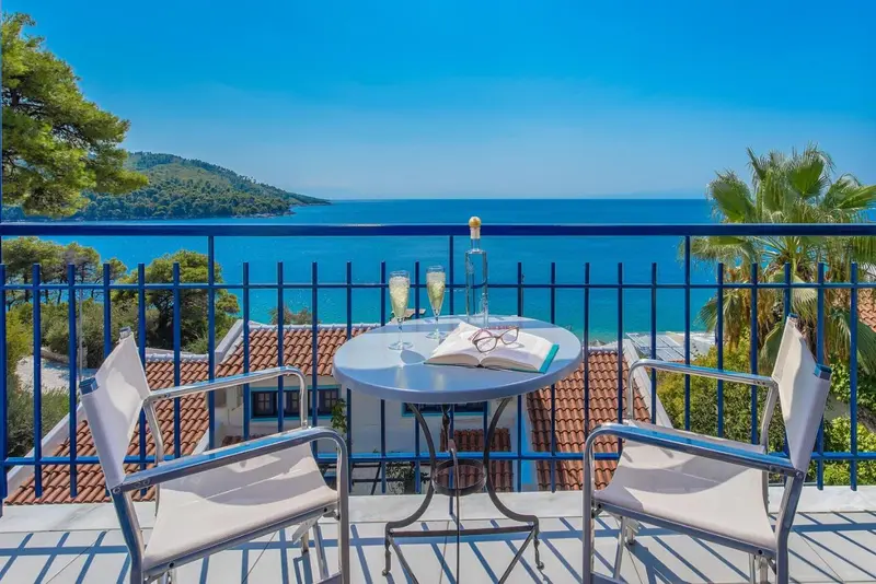 Une table ronde avec des verres et un livre est posée sur un balcon avec vue sur la mer.