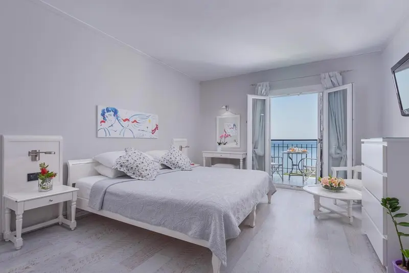 Chambre lumineuse avec un grand lit et un accès à un balcon donnant sur la mer.