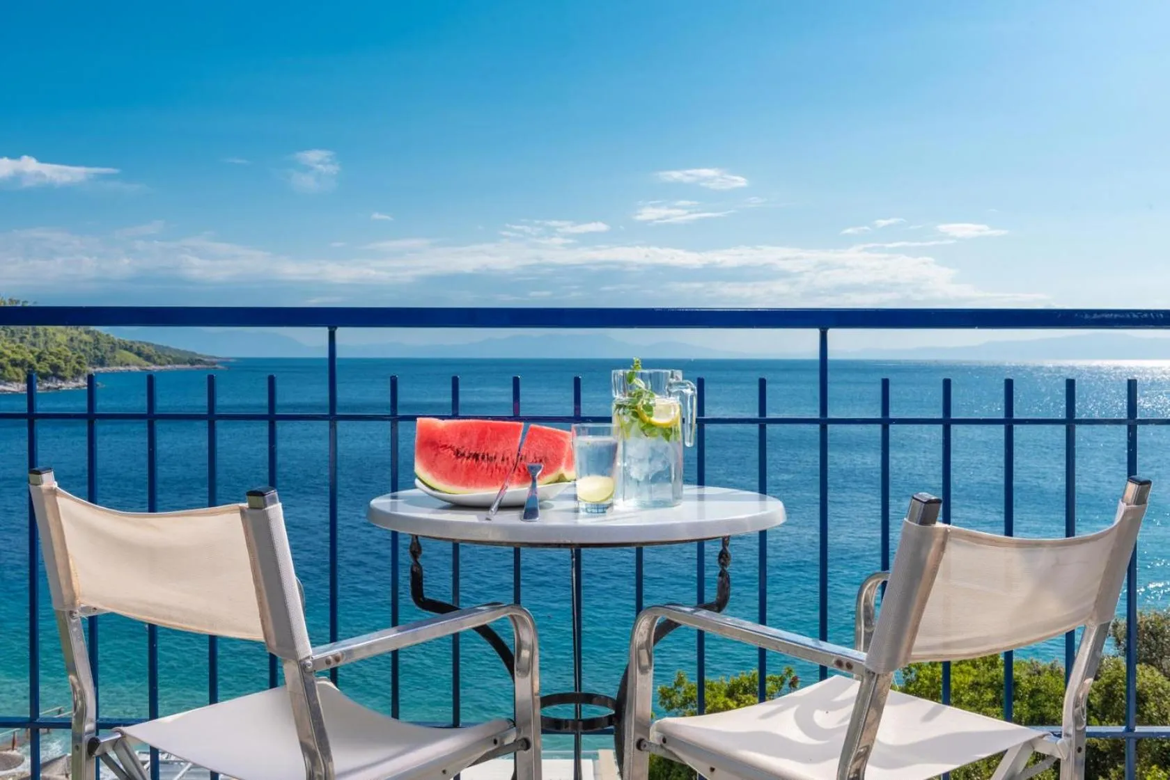 Une table avec des fruits et des boissons est mise en scène sur une terrasse avec vue sur la mer.