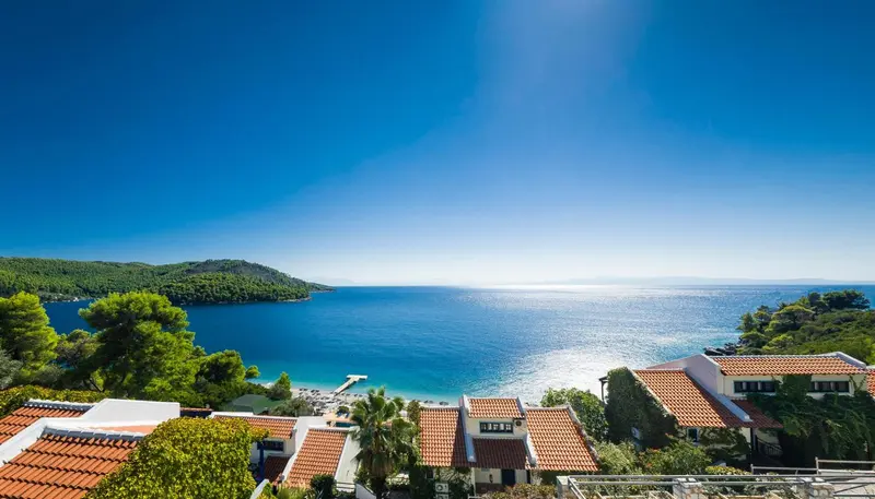 Vue aérienne sur une baie turquoise bordée de bâtiments aux toits en tuiles.