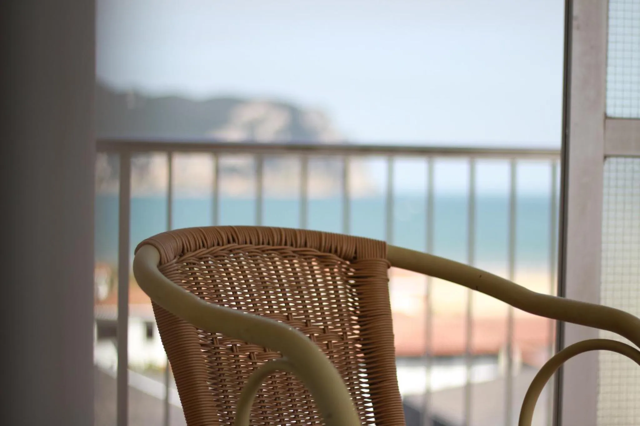 Fauteuil en osier sur une terrasse avec vue sur la mer et le littoral.