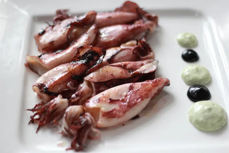 Assiette de calamars grillés avec une sauce verte et des olives.