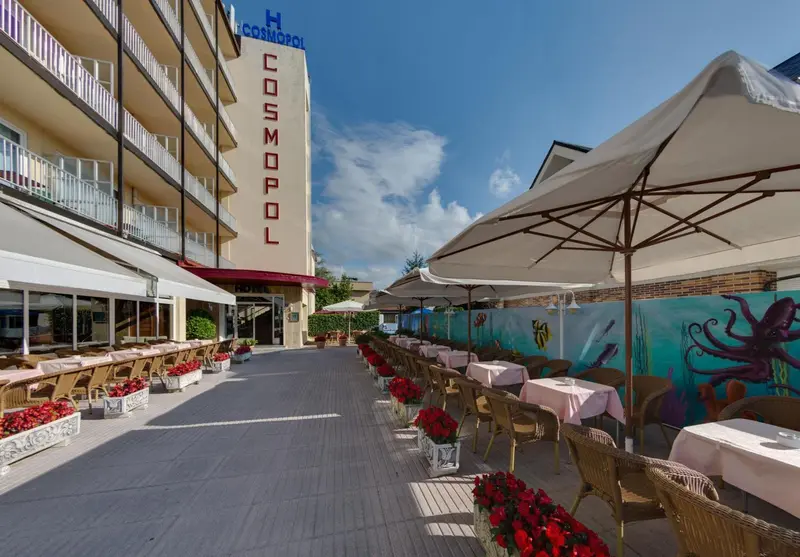 Terrasse ombragée avec tables et chaises devant un bâtiment.