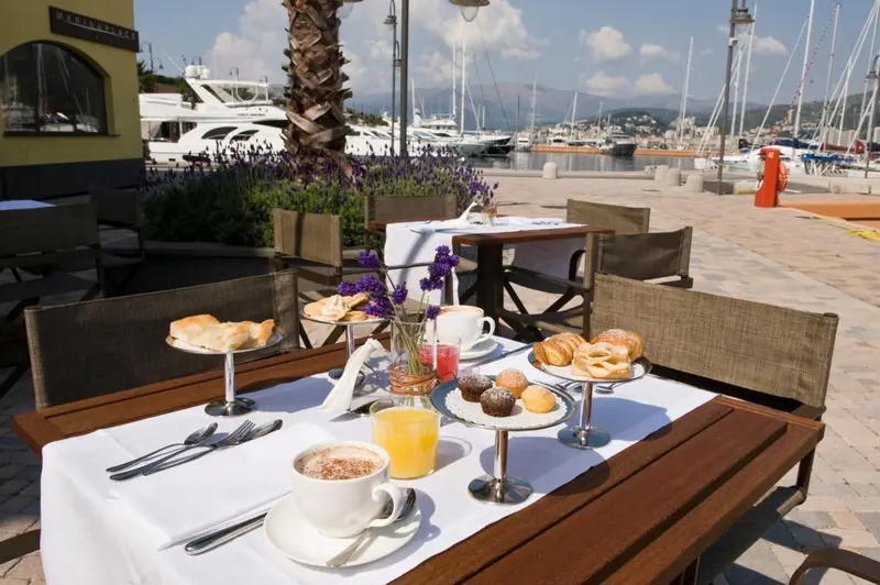 Une table dressée pour le petit-déjeuner en terrasse avec vue sur un port de plaisance.