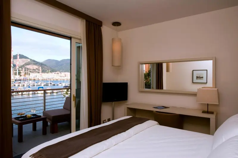 Chambre lumineuse avec vue sur un port de plaisance et des montagnes.