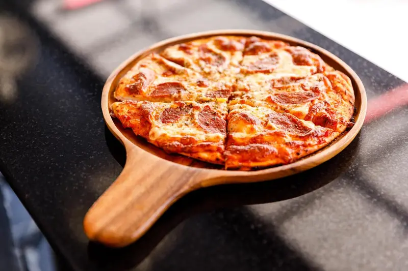 Une pizza pepperoni est présentée sur une planche à pizza en bois.