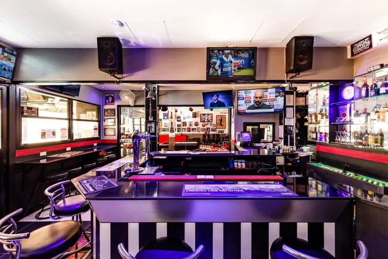 Un comptoir de bar illuminé avec des tabourets et des écrans de télévision.