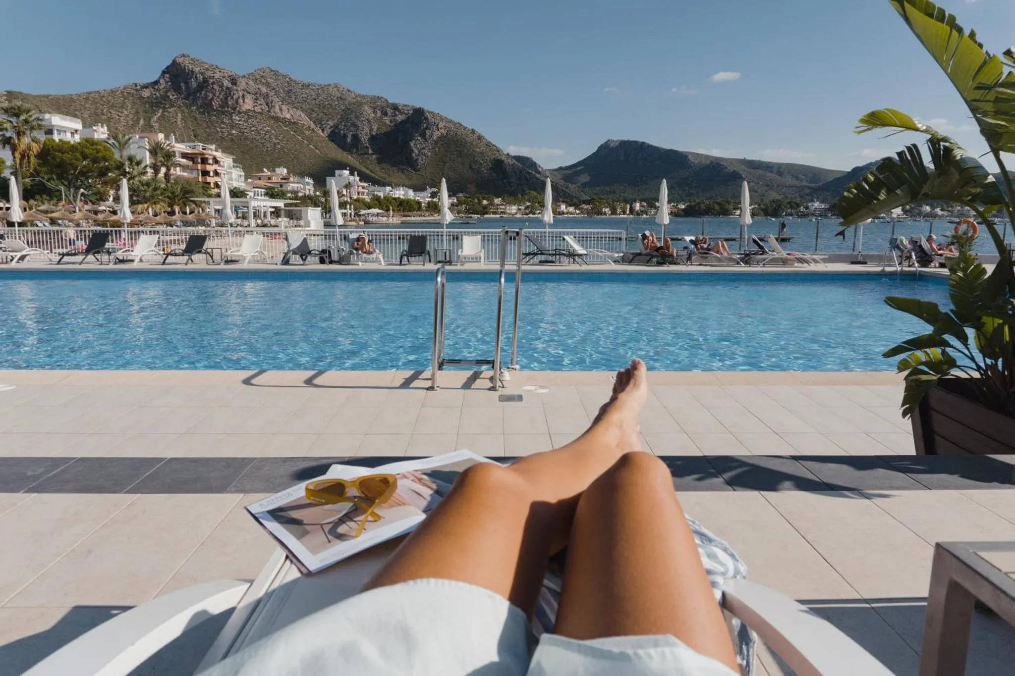 Une personne se relaxe au bord d'une piscine ensoleillée avec vue sur la mer et les montagnes.