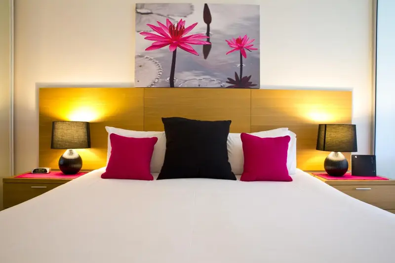 Un lit blanc avec des oreillers roses et noirs dans une chambre lumineuse.