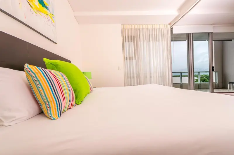 Un lit avec des oreillers colorés dans une chambre lumineuse donnant sur une vue extérieure.