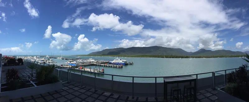 Vue panoramique sur une marina et des montagnes verdoyantes sous un ciel nuageux.