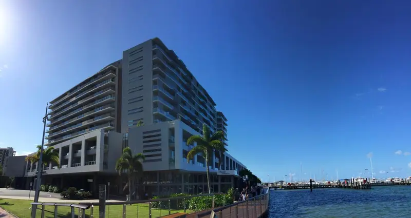 Bâtiment moderne avec des balcons donnant sur l'eau et une végétation tropicale.