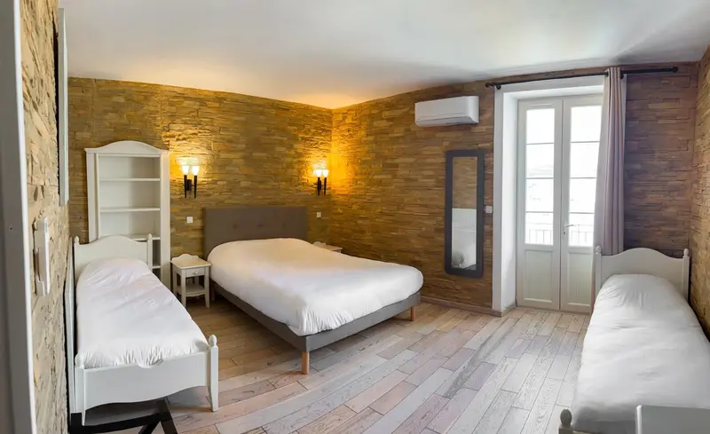 Une chambre lumineuse avec trois lits et un mur en pierre.