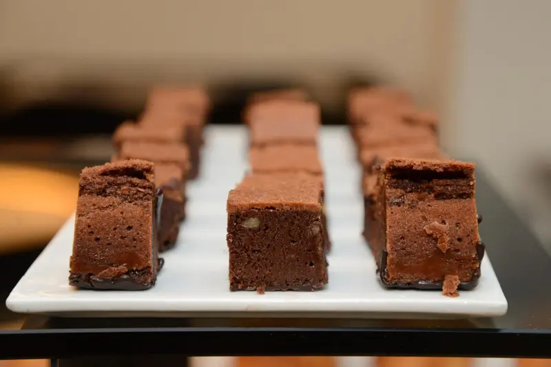 Présentation de carrés de brownie sur un plat blanc.