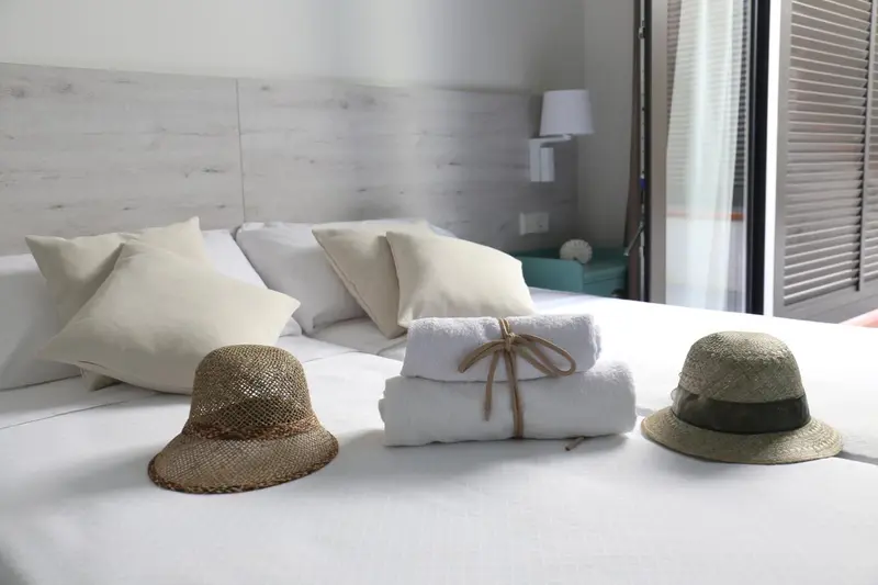 Un lit recouvert de draps blancs et d'oreillers, décoré de chapeaux de paille et de serviettes enroulées.