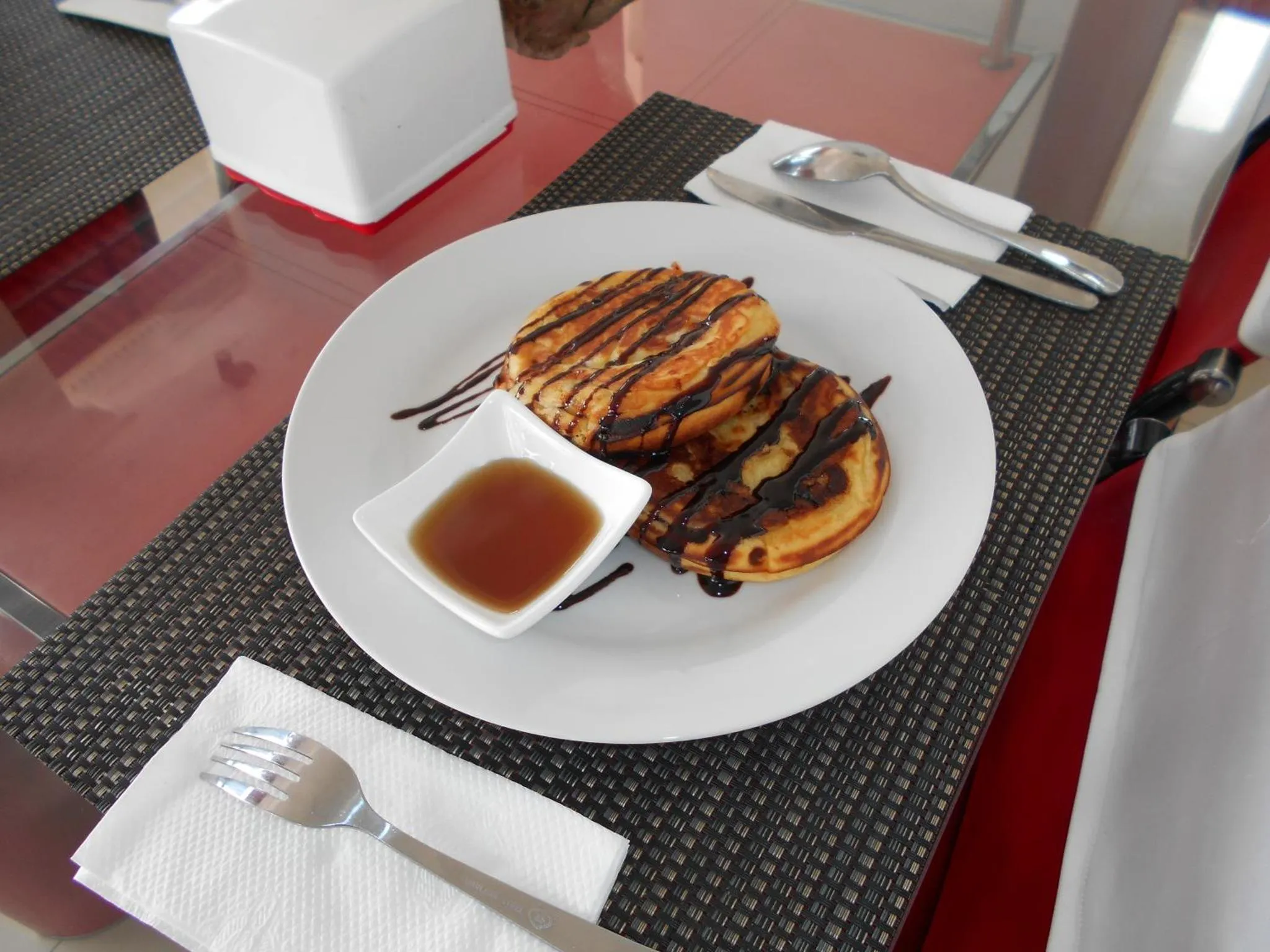 Assiette de crêpes décorées de chocolat et accompagnées d'un pot de sirop.