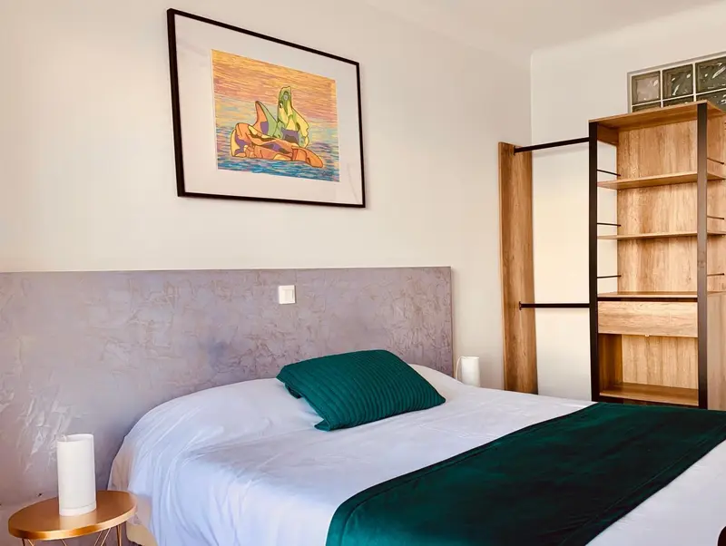 Une chambre avec un lit recouvert d'une couette blanche et d'une couverture verte, et une décoration murale.
