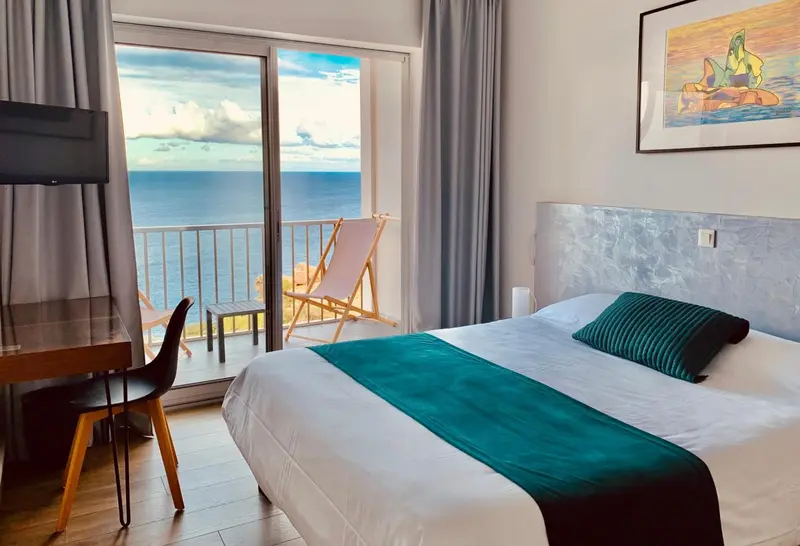 Une chambre lumineuse avec un lit et un bureau donnant sur une vue mer.