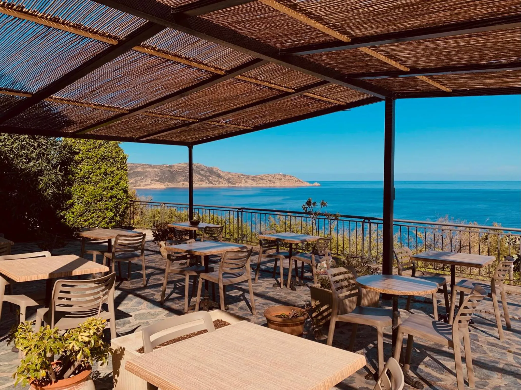 Terrasse ombragée avec tables et chaises donnant sur la mer.