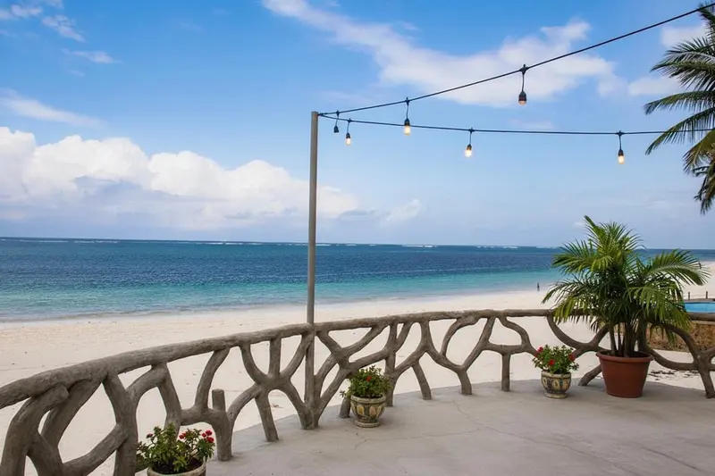Terrasse en pierre avec végétation donnant sur une plage de sable blanc et la mer.