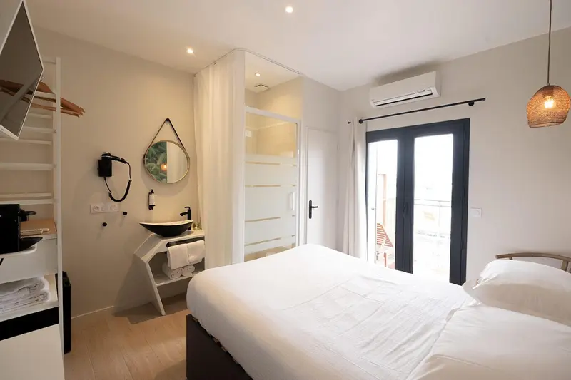 Une chambre lumineuse avec un lit blanc et une salle de bain attenante.