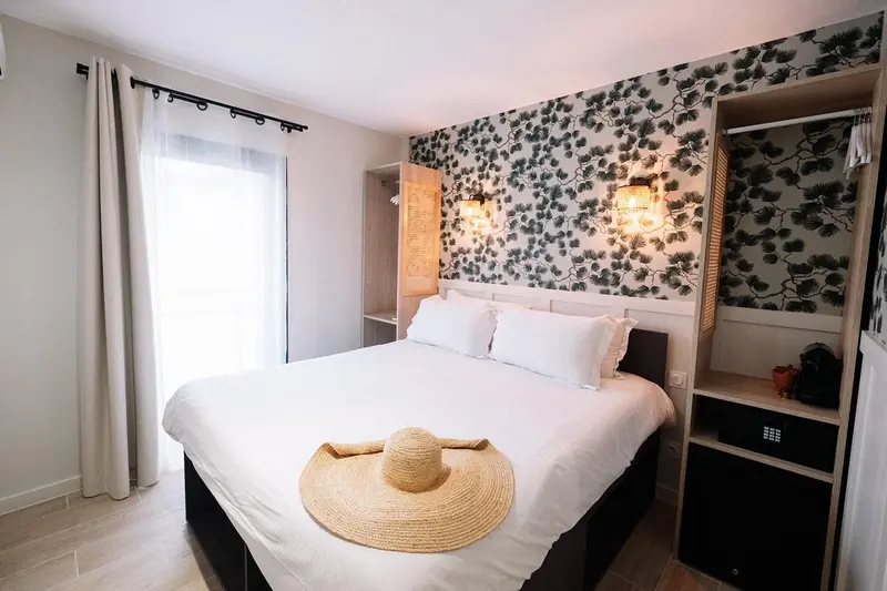 Une chambre lumineuse avec un lit recouvert d'une courtepointe blanche et d'un chapeau de paille.