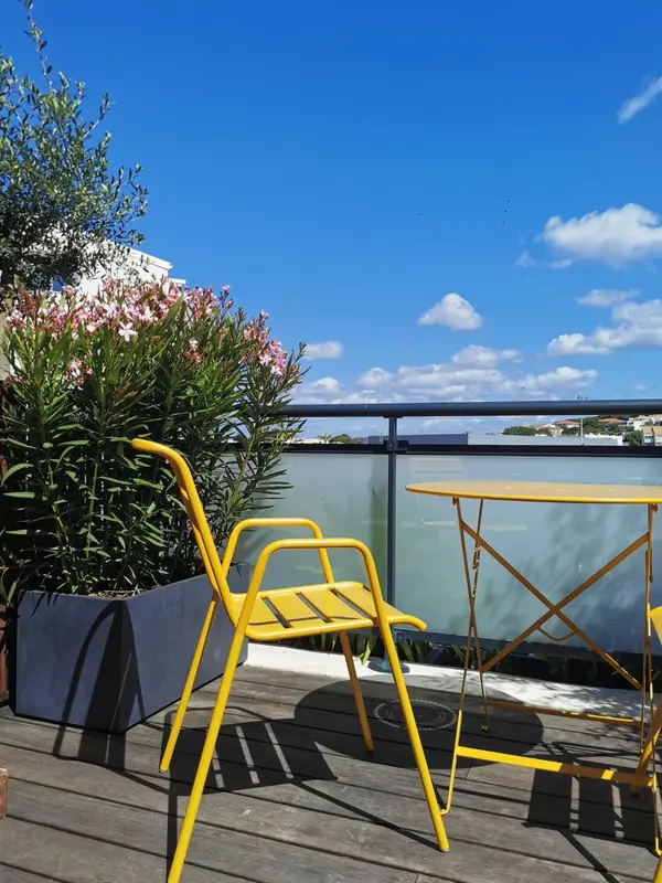 Terrasse ensoleillée avec mobilier jaune et vue sur la mer.
