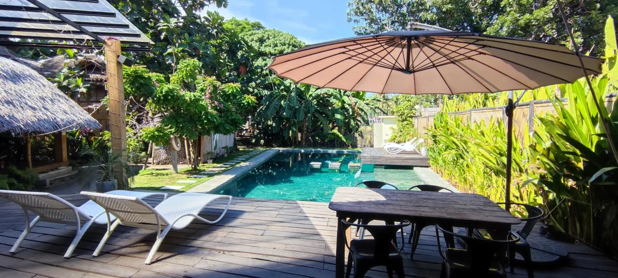 Terrasse en bois avec transats et table près d'une piscine rectangulaire.
