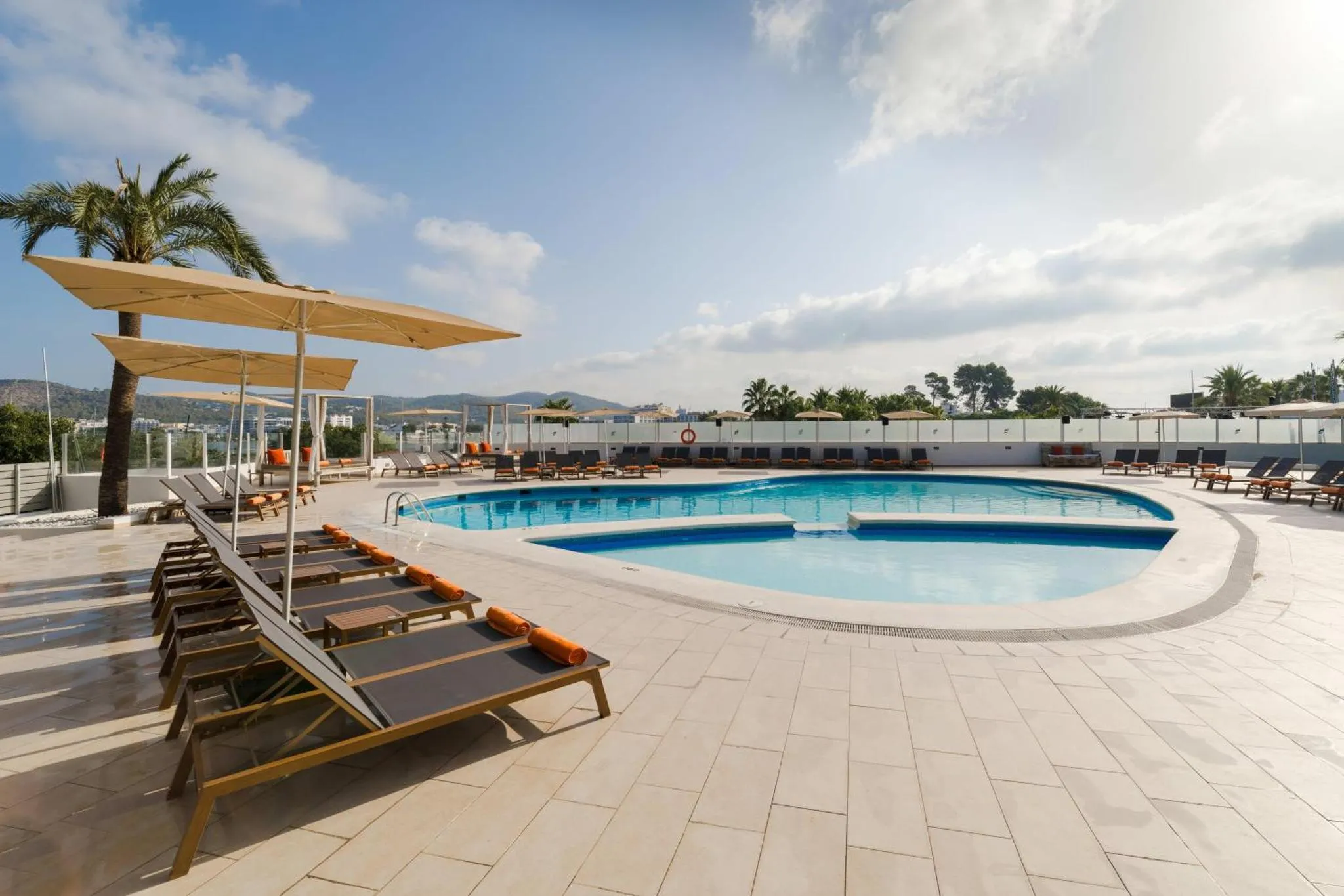 Transats alignés au bord d'une piscine ensoleillée avec une vue sur la mer.