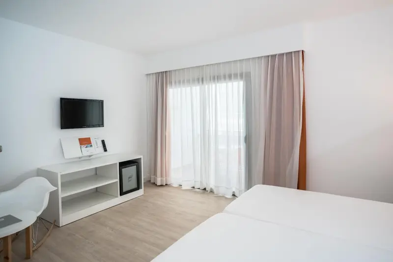 Une chambre lumineuse avec un grand rideau blanc et un téléviseur mural.