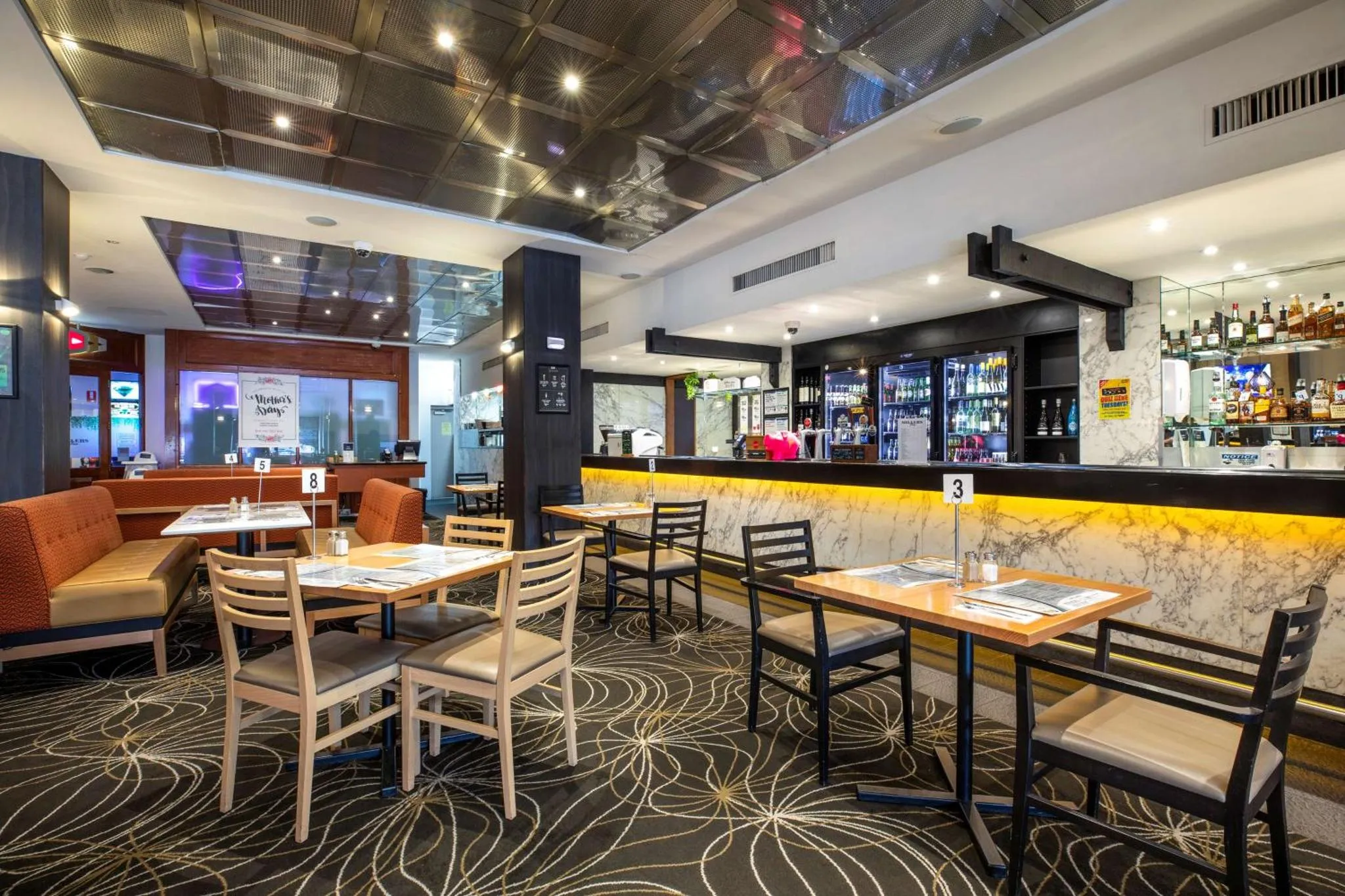 Une salle lumineuse avec des tables et des canapés, un comptoir de bar et des bouteilles exposées.