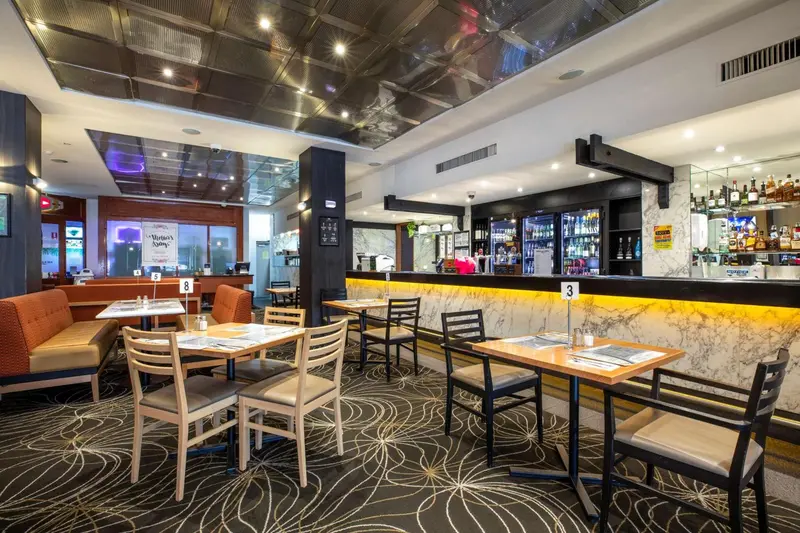 Une salle lumineuse avec des tables et des canapés, un comptoir de bar et des bouteilles exposées.