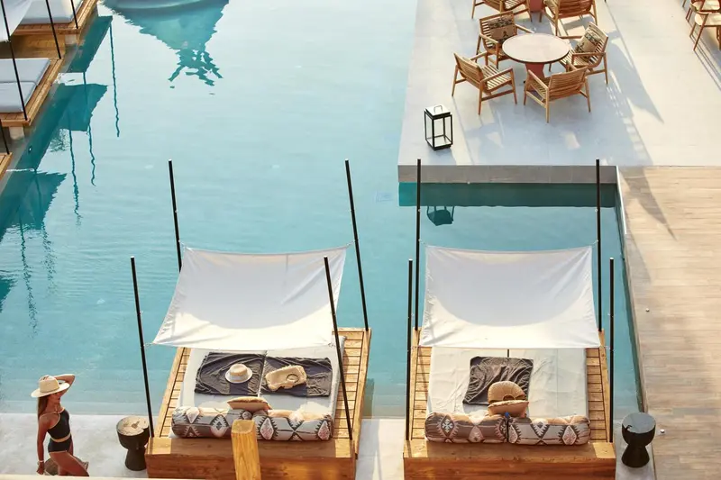 Deux lits de soleil avec parasols blancs bordent une piscine turquoise.