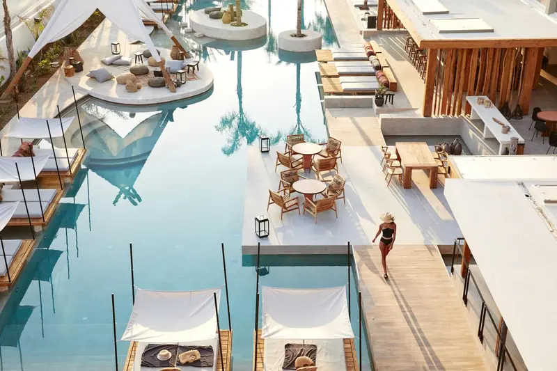 Vue aérienne d'une piscine sinueuse bordée de transats et de parasols blancs.